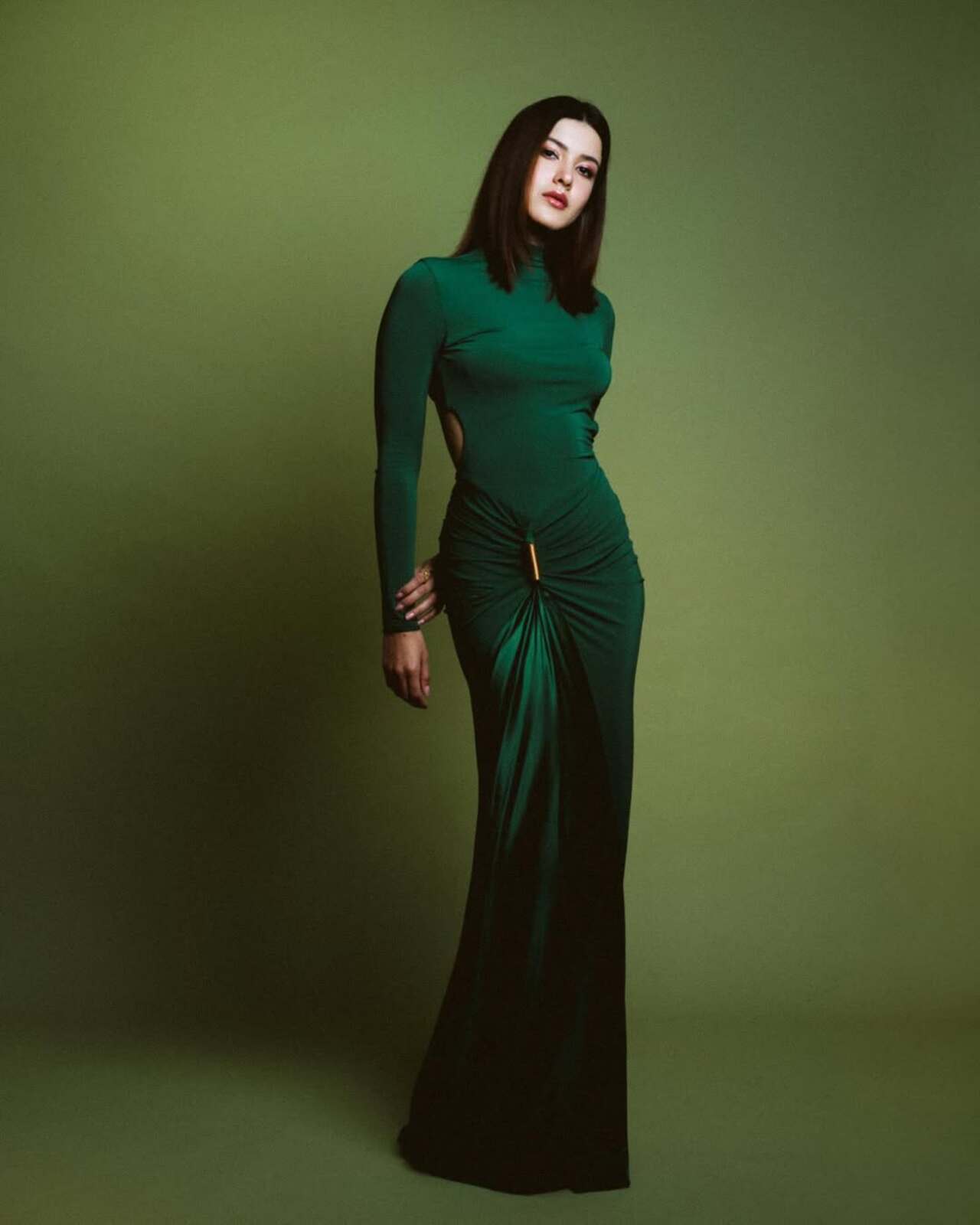<p>Shanaya opts for a striking emerald-green bodycon gown featuring a high neckline and full sleeves, exuding understated drama. The silhouette is elevated with a subtle side cut-out and ruched detailing at the waist, cinched with a metallic accent that adds structure. The floor-length hem and monochrome green backdrop amplify the look&rsquo;s sleek, almost mysterious appeal&mdash;perfectly aligning with the film&rsquo;s moody aesthetic</p>